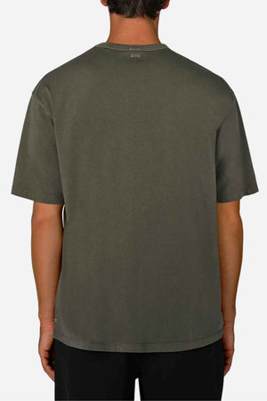 An individual is wearing the Industrie The Del Sur Tee in an oversized fit and olive green, positioned with their back to the camera. Made from 100% cotton, this short-sleeved shirt complements black pants effortlessly. The backdrop is a solid light gray color, highlighting a casual yet stylish appearance.