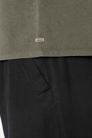 Close-up image showcasing the bottom of an olive-green, oversized Industrie The Del Sur Tee with a small tag on the seam. Crafted from 100% cotton, this stylish piece pairs perfectly with black pants.