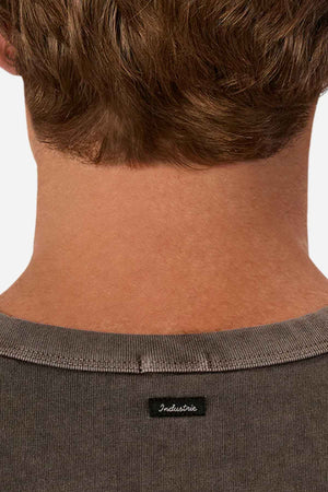 A close-up photo features the back of a person’s head and neck, accentuating their oversized gray tee known as "The Del Sur Tee" by Industrie. The black tag prominently displays "Industrie," while their short brown hair complements the simplicity of this 100% cotton shirt.
