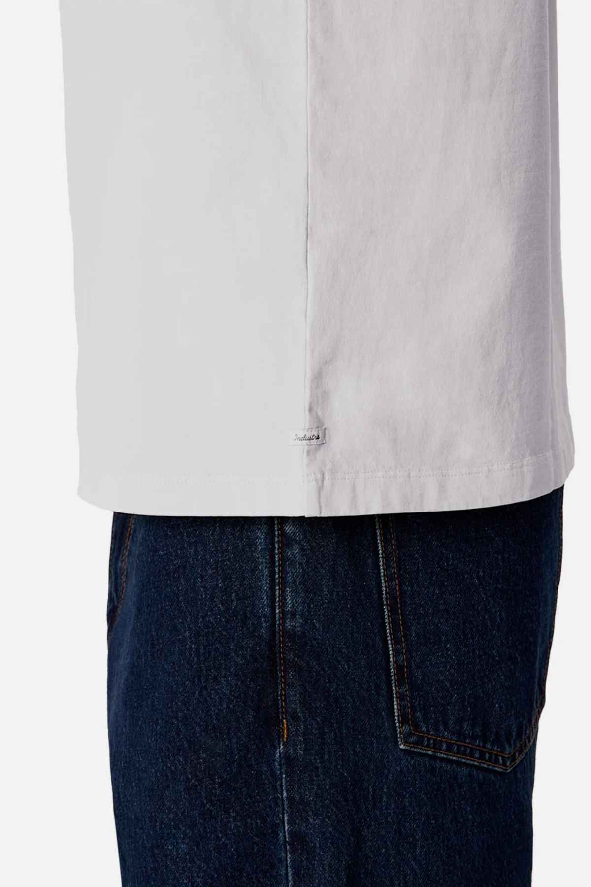 Close-up of a person wearing the Industrie The Del Sur Tee, an oversized fit, white 100% cotton T-shirt, paired with dark blue jeans. The focus is on the side seam of this comfortable tee, which features a small tag. The jeans showcase a visible back pocket.