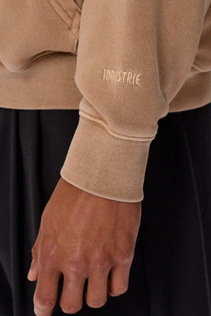 Close-up of a person wearing the Industrie The Del Sur Washed Hoodie in an oversized camel fit, featuring "INDUSTRIE" embroidered on the sleeve, paired with black pants.