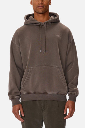A person in a loose-fitting, acid wash hoodie and dark pants stands against a white background. The Industrie "The Del Sur Washed Hoodie" features a front pocket, drawstrings, and subtle embroidered text on the chest and sleeve.