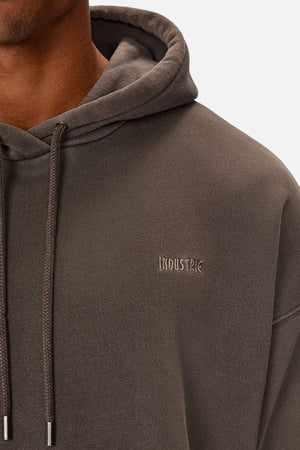 A person wears the Industrie The Del Sur Washed Hoodie in dark gray, featuring sleek "INDUSTRIE" embroidery on the chest. With the hood down and drawstrings hanging in front against a white backdrop, its subtle acid wash adds modern edge to the classic design.