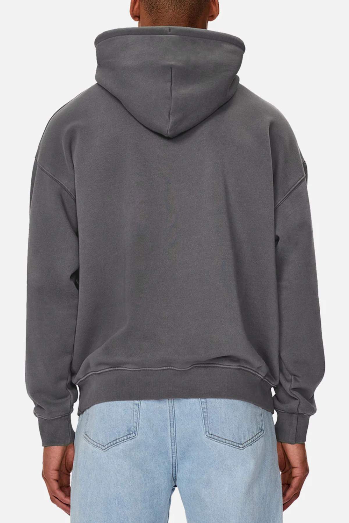 A person is seen from the back wearing the Industrie The Del Sur Washed Hoodie in dark gray, styled with light blue jeans. The oversized hoodie has its hood up and their hands rest by their sides against a plain white backdrop.