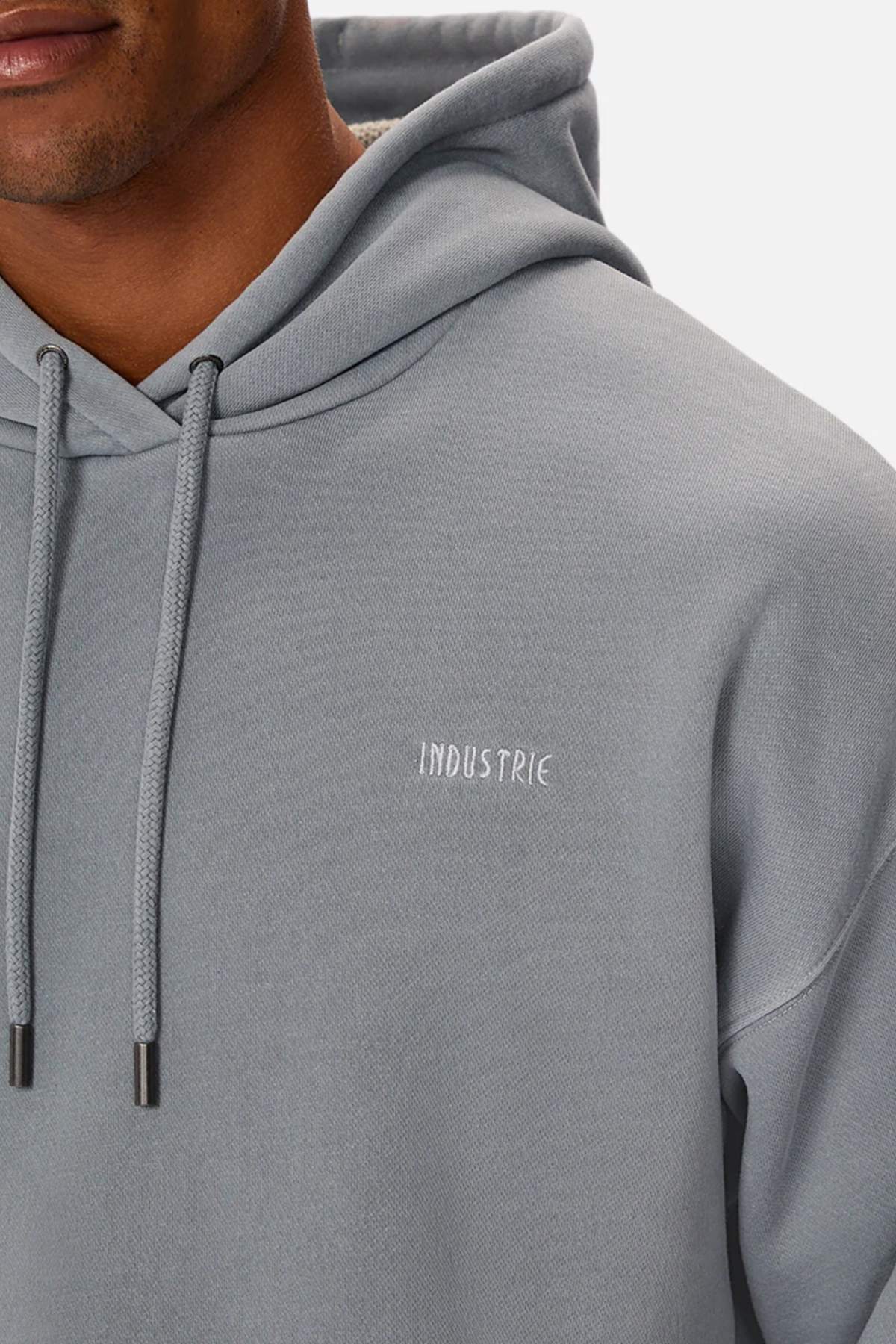 A person wears the Industrie The Del Sur Washed Hoodie in light gray with drawstrings and "INDUSTRIE" subtly embroidered on the chest; only their lower face and upper torso are visible.