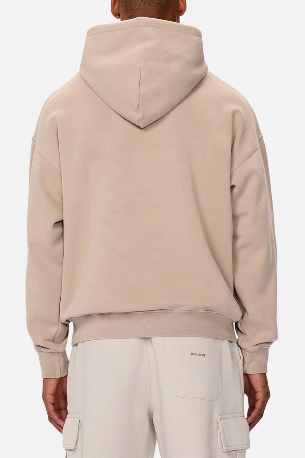 Dressed in an Industrie The Del Sur Washed Hoodie and matching pants, a person faces away, showcasing the hood up on the oversized beige hoodie with its loose fit. Large pockets highlight the pants against a plain white background, emitting an effortless casual style.