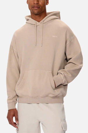 A man wears the oversized Industrie The Del Sur Washed Hoodie, subtly printed with "DISTRICT" on the chest. It features a front pocket and drawstrings, perfectly complementing his light-colored pants as he stands against a plain background.