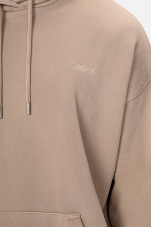 A person wears an oversized, soft beige hoodie with drawstrings. The Del Sur Washed Hoodie features "INDUSTRIE" embroidered subtly on the chest, offering a cozy and inviting fit.