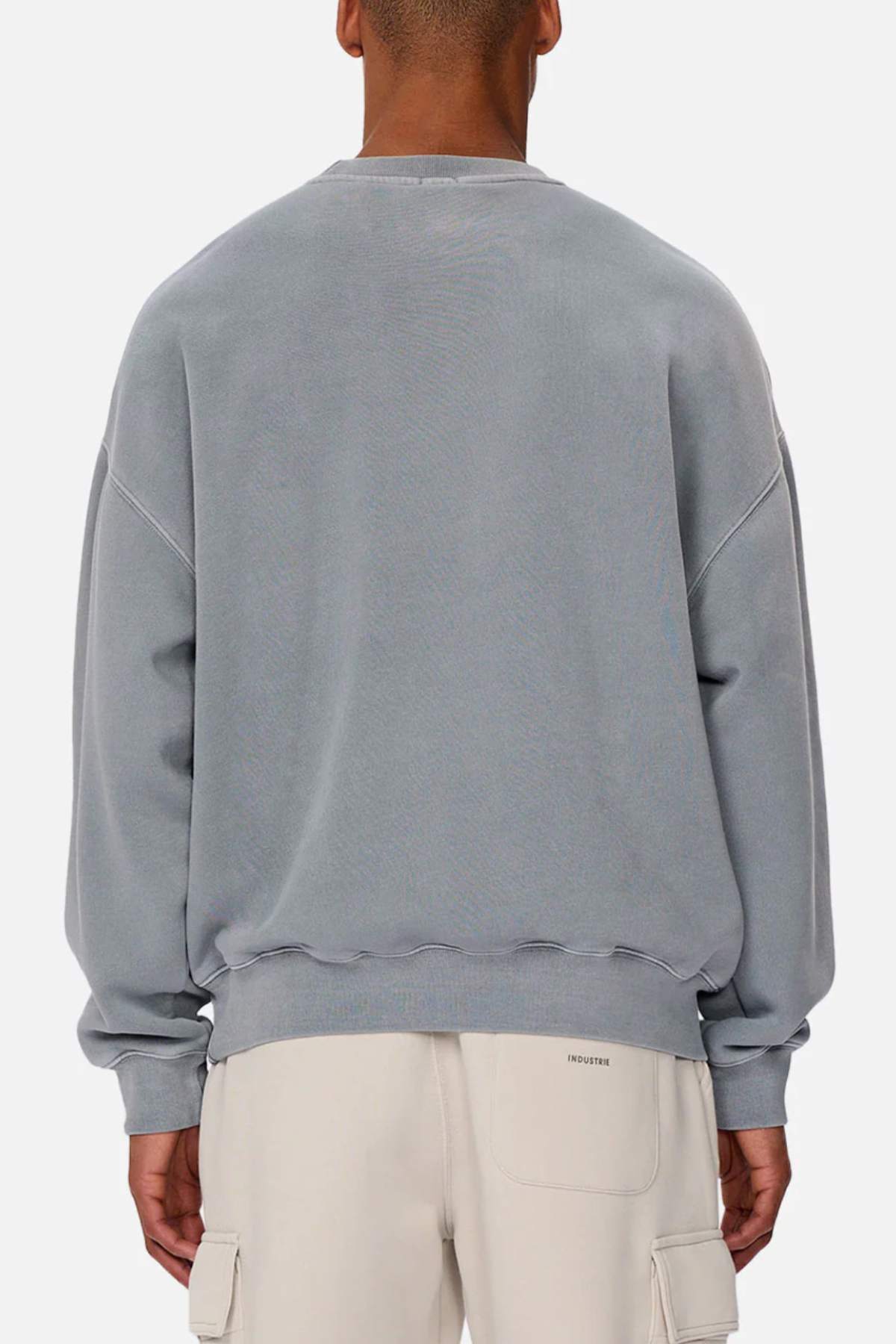 A person is shown from behind wearing an oversized light gray Industrie The Del Sur Washed Sweat with rib knit cuffs and off-white cargo pants, against a plain light background with "INDUSTRIE" on the back of the pants.
