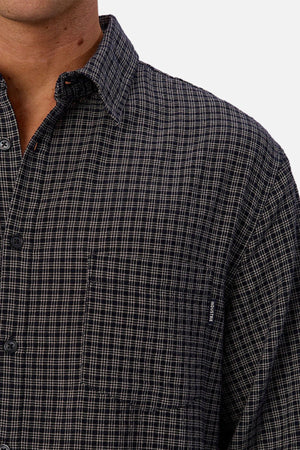 A close-up of a person wearing the Industrie The Diego Long Sleeve Shirt, featuring a dark checked pattern and front pocket. Only the lower face, neck, shoulder, and upper chest are seen against a white background.