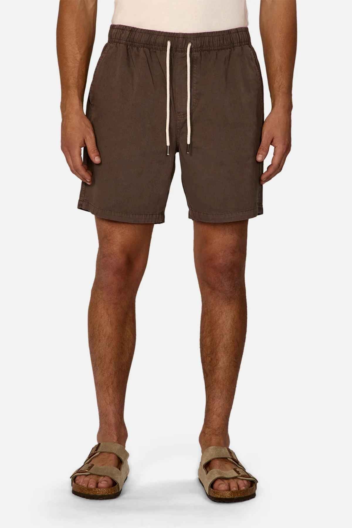 A person stands against a white background, wearing the Industrie The Dublin Short, a summer staple featuring a drawstring and elasticized waistband. They're paired with backless Birkenstock-style sandals, with their hands resting casually at their sides.