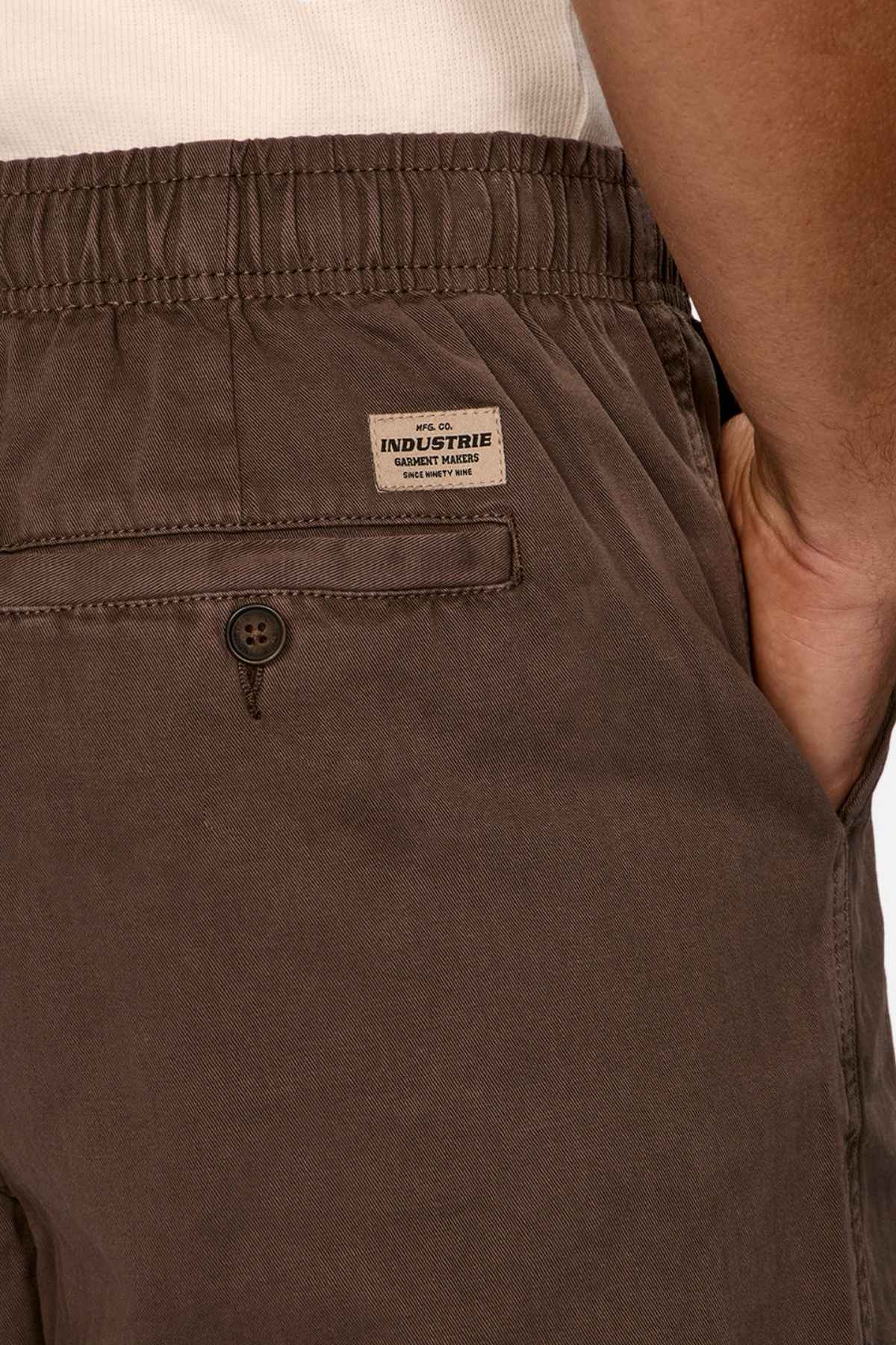 A detailed look at an individual sporting Industrie The Dublin Short, showcasing a brown elasticized waistband and a button-up back pocket. The label "Industrie Clothing" is visible. Paired with a tucked-in white shirt, this outfit is the quintessential summer essential.