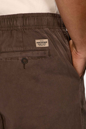 A detailed look at an individual sporting Industrie The Dublin Short, showcasing a brown elasticized waistband and a button-up back pocket. The label "Industrie Clothing" is visible. Paired with a tucked-in white shirt, this outfit is the quintessential summer essential.