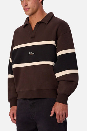 Someone wears the Industrie The Eastbourne Tracktop in dark brown with black and cream horizontal stripes, a camp collar, long sleeves, a chest logo, and a relaxed fit, paired with dark pants.