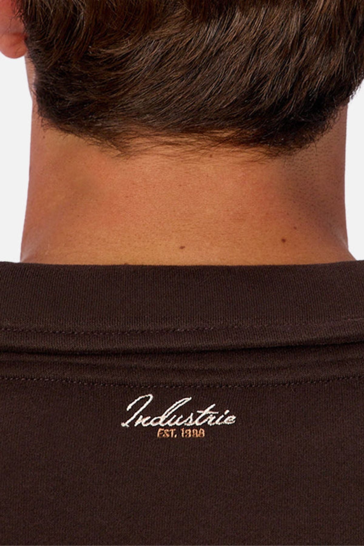 Close-up of the back and neck, showcasing a dark brown Industrie The Eastbourne Tracktop with "Industrie EST. 1999" embroidered in white near the camp collar for a relaxed silhouette.