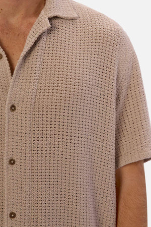 Close-up of a person in Industrie The Egnazia Short Sleeve Shirt in beige with dark buttons. Made from breathable linen-cotton, it features a waffle-knit pattern. The photo highlights the upper torso and shoulder, making it perfect for any summer wardrobe.