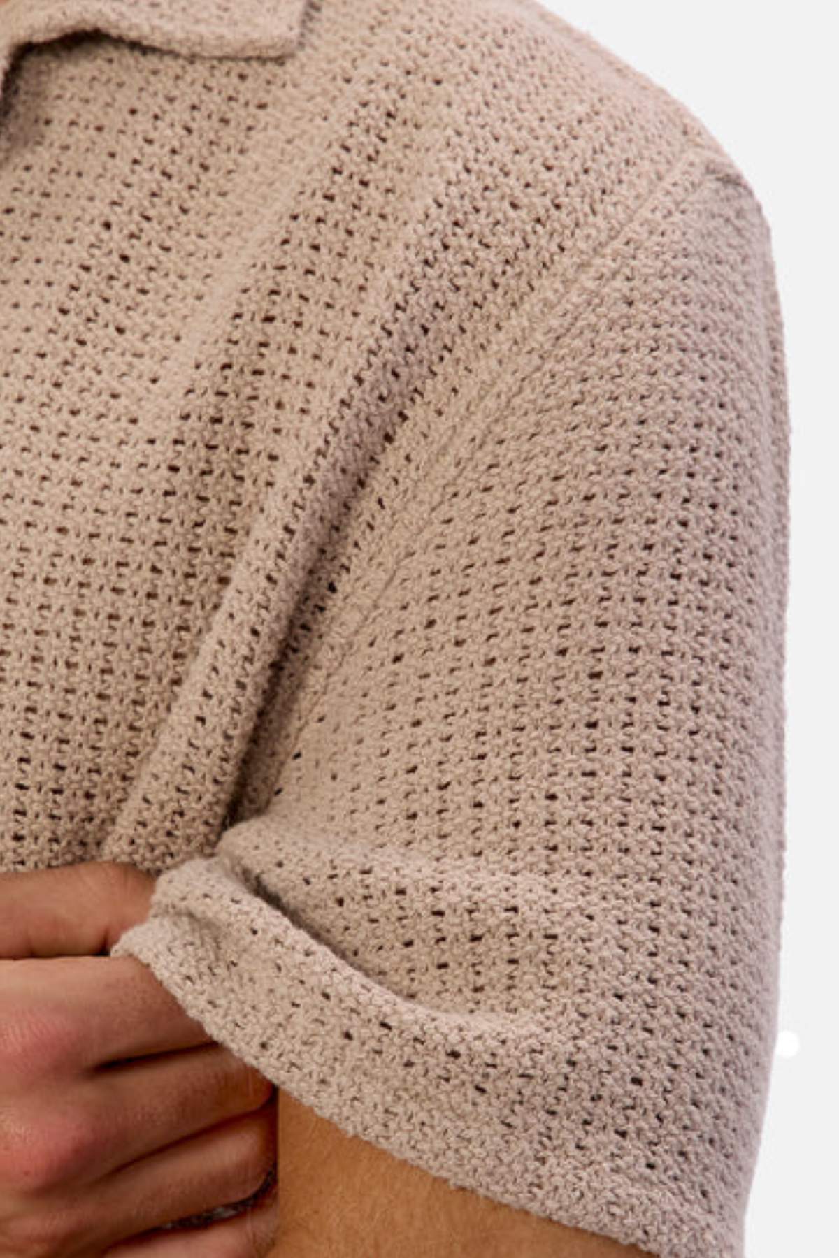 Close-up of the Industrie The Egnazia Short Sleeve Shirt in beige. This linen-cotton blend features a detailed textured pattern and rolled-up sleeves, with a hand partly visible holding the sleeve. Ideal for your summer wardrobe.
