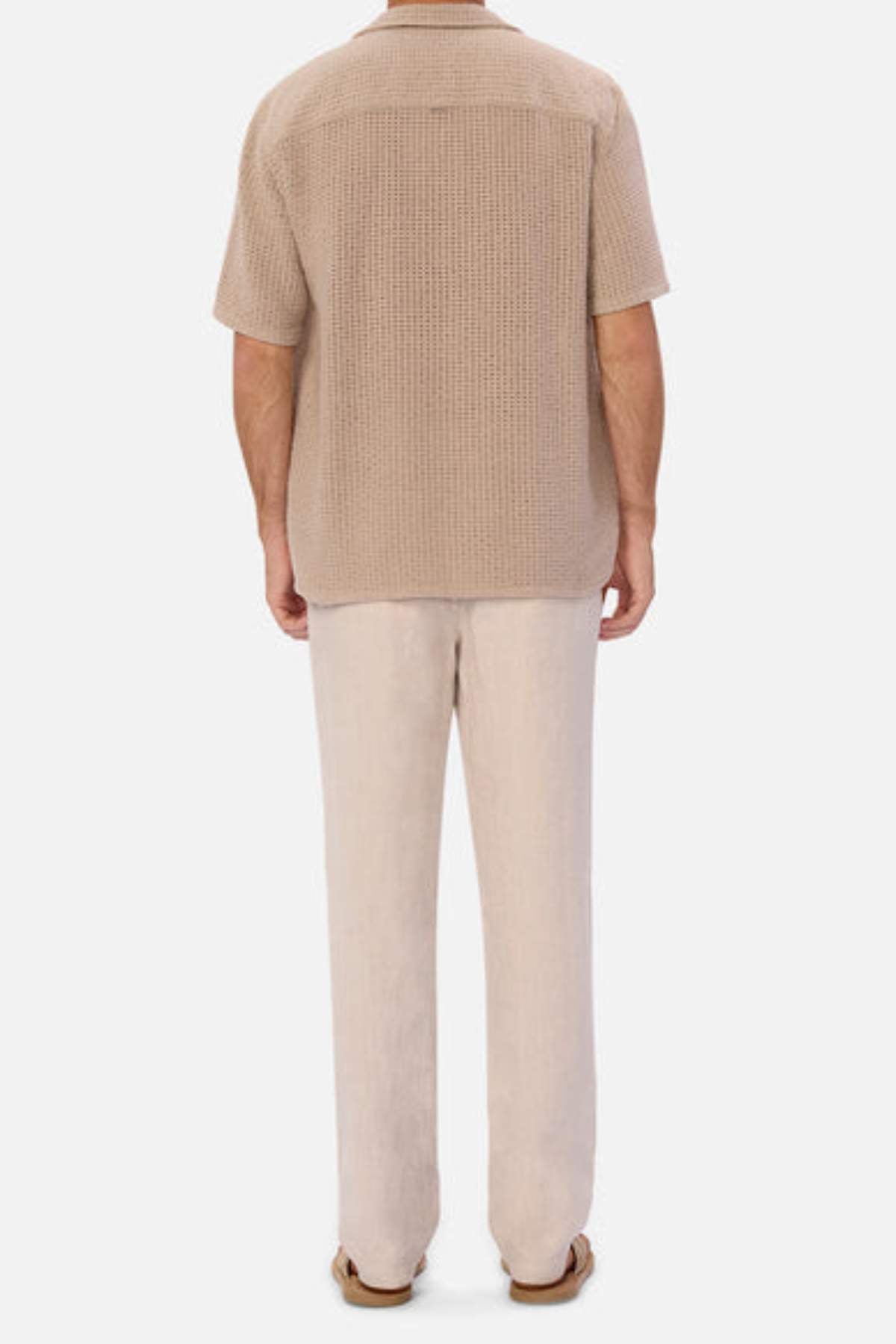 Rear view of a person against a white backdrop in the breathable Industrie The Egnazia Short Sleeve Shirt, textured beige and made from a linen-cotton blend. Light pants and brown sandals complete this ideal summer look.