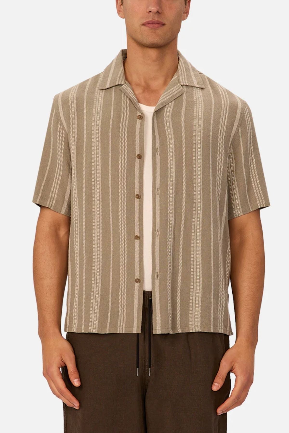 A person wearing the Industrie The Fabriano Short Sleeve Shirt—beige with vertical white stripes—over a white undershirt and brown pants, standing against a plain background.
