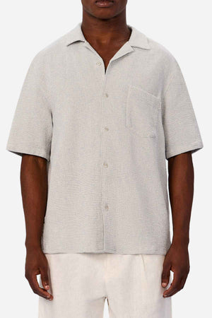 A person wears the Industrie The Franklin Short Sleeve Shirt—light gray, breathable cotton with a camp collar and chest pocket—paired with off-white pants, standing against a plain white background.