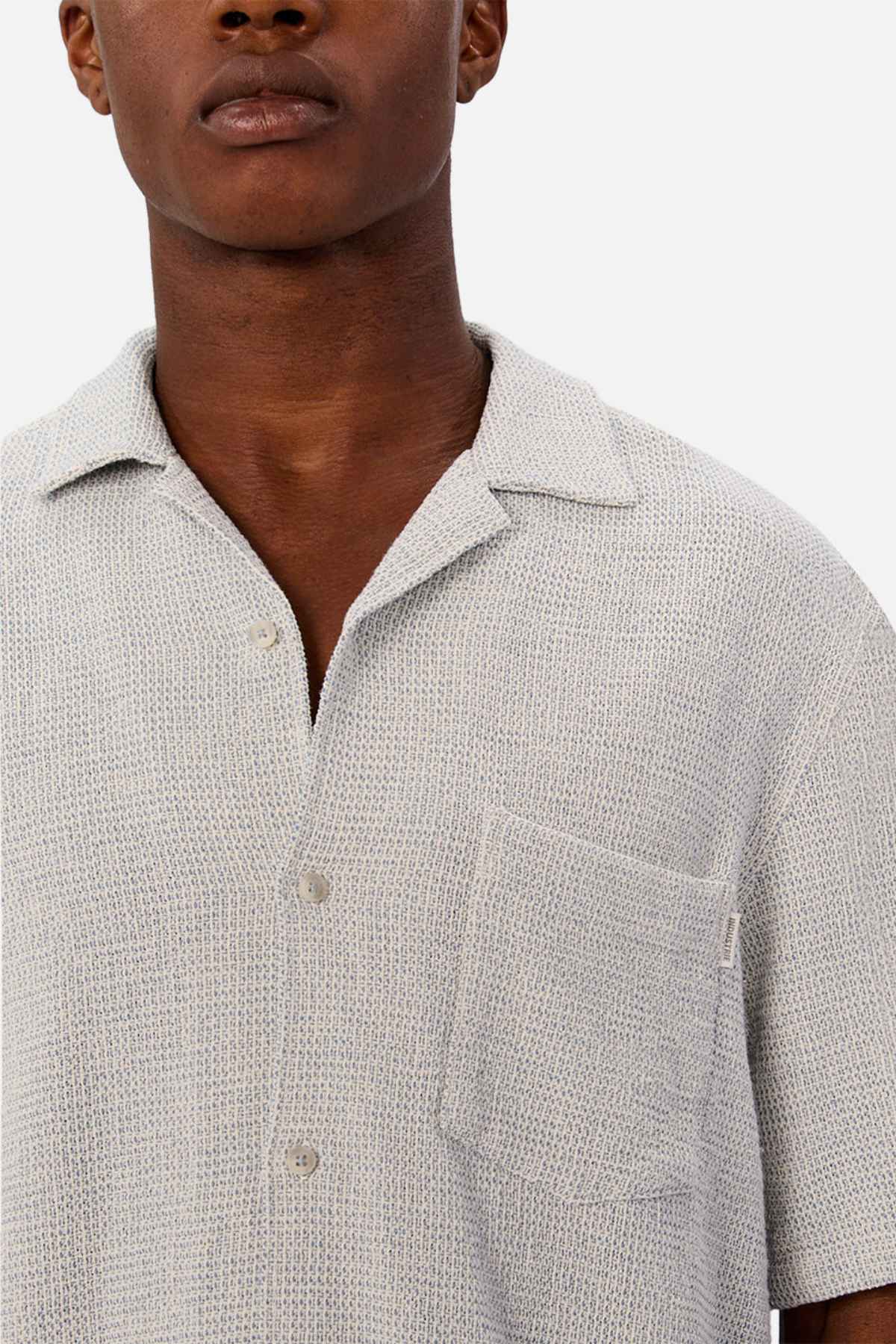 A person wears the Industrie The Franklin Short Sleeve Shirt, a light grey textured casual camp collar shirt with a front pocket, shown from shoulders to mid-chest against a plain white background.