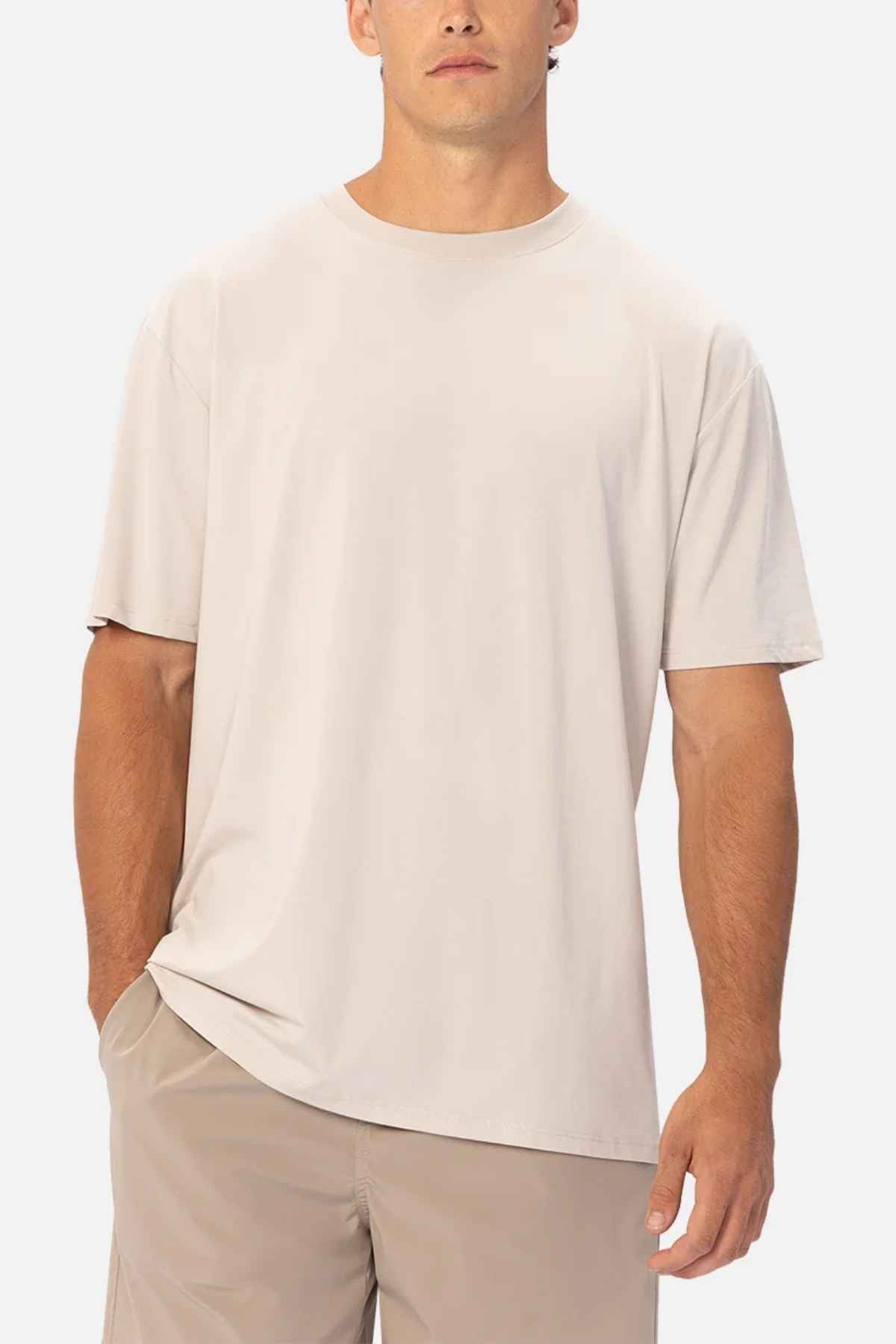 A man wearing a plain beige Industrie The Freeman Athletic Tee and khaki athletic shorts stands against a white background. One hand is in his pocket, and he is facing forward.