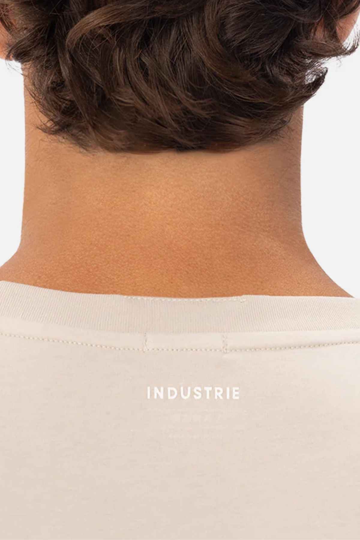 Back view of a person wearing the Industrie The Freeman Athletic Tee in a light color, featuring "INDUSTRIE" printed on the collar. The person's hair is curly and brown.