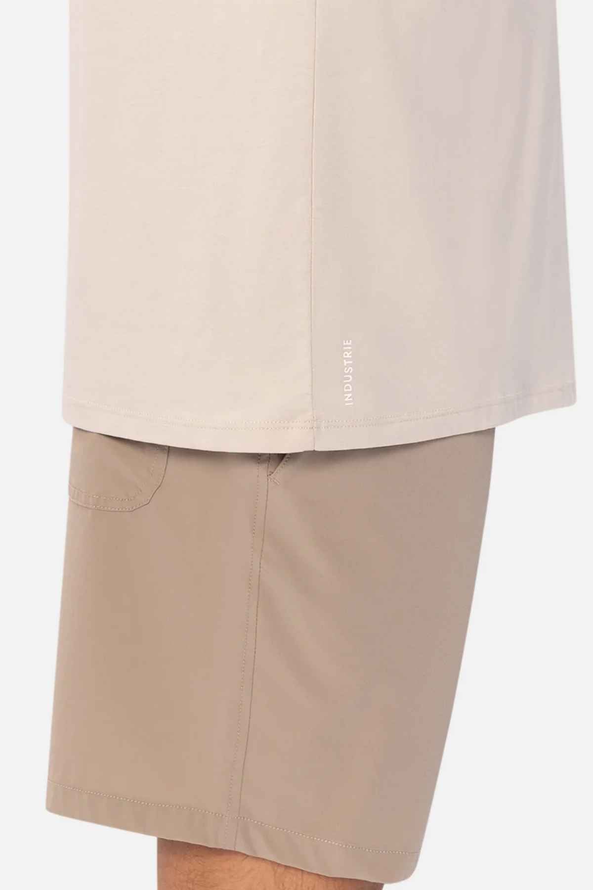 Close-up of a person wearing a light beige "Industrie The Freeman Athletic Tee," paired with tan shorts. The casual outfit highlights simplicity and comfort, with the image focusing on the clothing details.