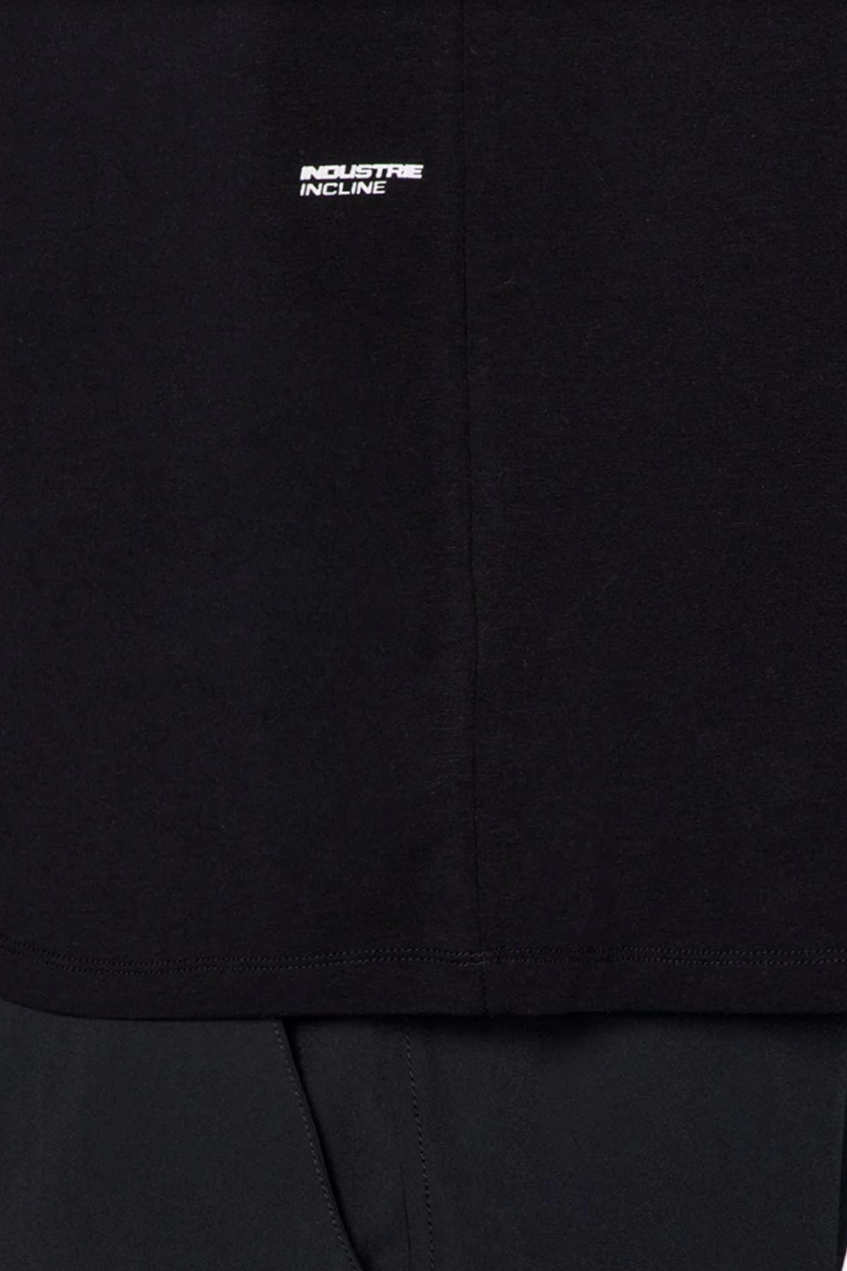 Close-up of the Industrie The Freeman Sleeveless Tee in black, featuring a small white "INDUSTRIE INCLINE" logo on the chest, center seam detail, and quick-dry technology—styled with dark pants, ideal for workouts.
