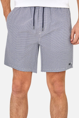 A person wears the Industrie The Freeport Bahama Short in white and navy blue striped seersucker, featuring an elasticised drawcord waist, pockets with hands inside, and a small left leg logo. Only part of the upper body is visible.