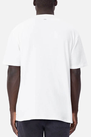 The person is wearing an oversized Industrie The Henderson Boucle Tee in plain white, seen from the back with hands relaxed. The soft grayish-white backdrop highlights the comfortable and relaxed style of this 100% cotton tee.