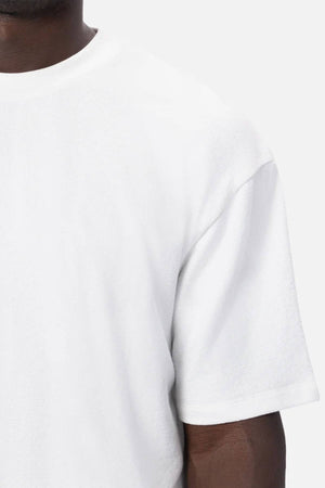 Close-up of a person in an oversized fit Industrie The Henderson Boucle Tee in plain white, highlighting the upper right section of the 100% cotton tee and part of their arm against a plain background.