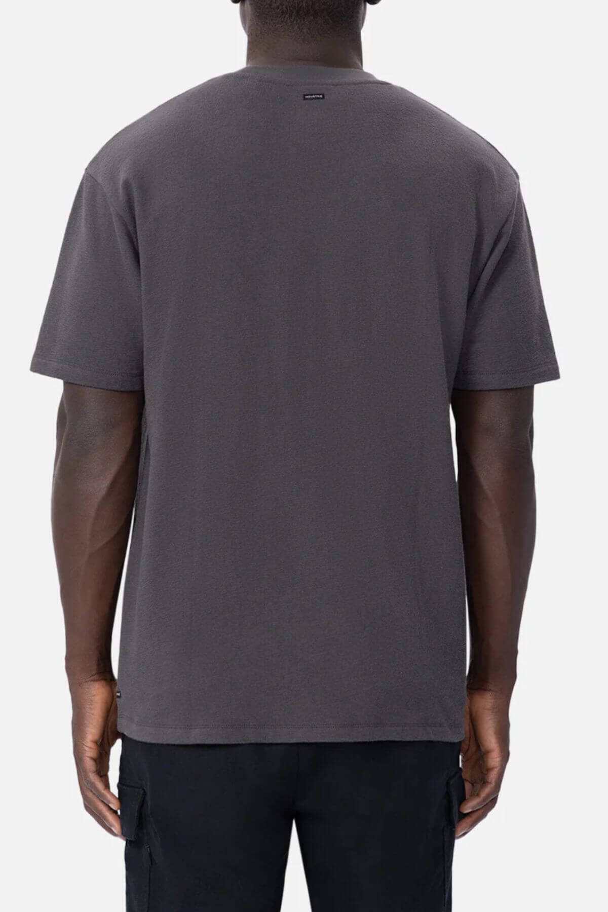 A person stands with their back to the camera, wearing an oversized Industrie The Henderson Boucle Tee in dark gray and black pants, set against a light gray background.