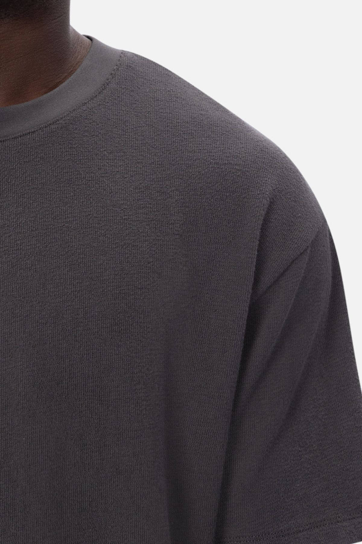 Close-up of a person wearing the Industrie The Henderson Boucle Tee, a dark gray, textured short-sleeve shirt. The shoulder, chest, and neck are visible against a plain white background.