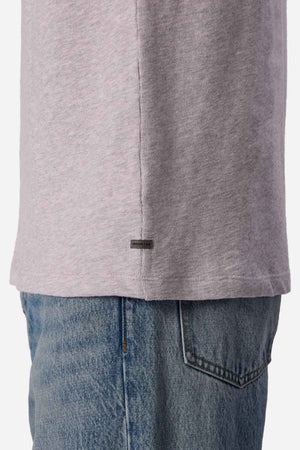 Side view of a person wearing a light gray Industrie The Henderson Boucle Tee paired with blue jeans. The emphasis is on the lower half of this oversized ensemble, highlighting a small rectangular tag with text. The texture and stitching of its 100% cotton fabric are clearly visible.