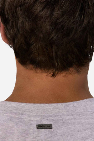 The image depicts the back of a person's head with short dark hair. They are dressed in an oversized, light gray shirt made entirely from cotton, featuring a small black label that reads "INDUSTRIE" on the back of the collar. This garment is similar to the Industrie The Henderson Boucle Tee style.