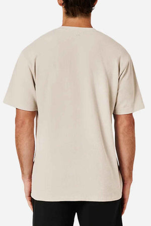 A person is seen from the back wearing an oversized look featuring the Industrie The Henderson Boucle Tee in beige paired with black pants. The plain, short-sleeved T-shirt is made from 100% cotton and set against a white background.