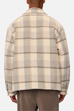 A person is seen from behind wearing the Industrie The Hillside Jacket, displaying its large plaid check in beige, cream, and gray. It is stylishly paired with brown pants against a white background.