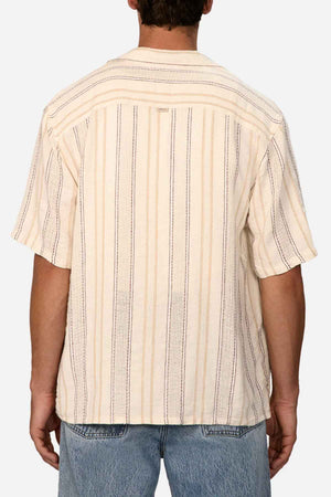 The individual is dressed in an Industrie The Lakeville Short Sleeve Shirt, made from a linen viscose blend and showcasing a textured stripe pattern in cream along with vertical blue and orange stripes. Positioned with their back to the camera, they are also sporting faded blue jeans against a simple white background.