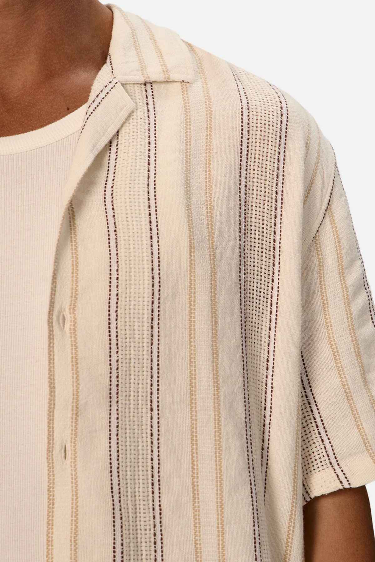 The Industrie Lakeville Short Sleeve Shirt is crafted from a linen viscose blend and showcases a textured stripe design layered over a ribbed cream tank top. Its partially unbuttoned style adds an air of casual elegance against a plain white background.