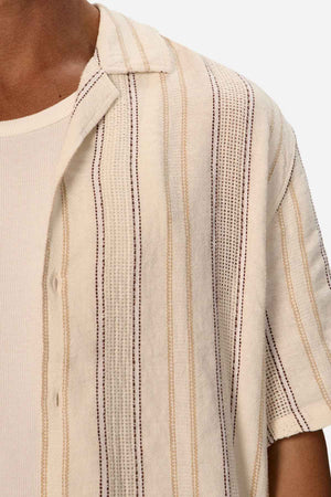 The Industrie Lakeville Short Sleeve Shirt is crafted from a linen viscose blend and showcases a textured stripe design layered over a ribbed cream tank top. Its partially unbuttoned style adds an air of casual elegance against a plain white background.