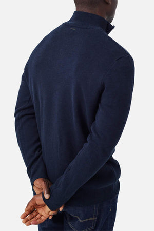 A person wearing the Industrie The Lakewood Zip Neck in dark blue, along with regular fit dark jeans, is shown from the back with their hands clasped behind them. Their head is turned slightly to the left against a plain white background.