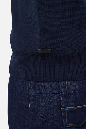 Close-up view of a person wearing dark blue jeans and the Industrie The Lakewood Zip Neck jumper in dark navy cotton, captured from the waist down. The image highlights the textures and colors of the clothing, with particular focus on the lower hem of the sweater and the pocket area of the regular fit jeans.