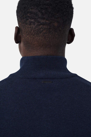 The image shows the back of a person's head and upper shoulders. The person is wearing an Industrie The Lakewood Zip Neck jumper in dark navy blue with a high collar and has short, closely-cropped hair. The background is plain and white.