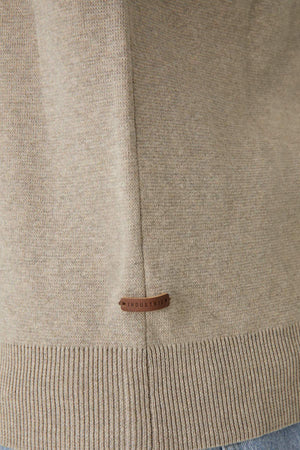 Close-up of the Industrie The Lakewood Zip Neck, a beige knitted cotton jumper featuring a ribbed hem and zip neck. A small brown leather tag with "INDUSTRIE" is sewn near the seam. The regular fit fabric has a smooth texture with subtle shading variations.