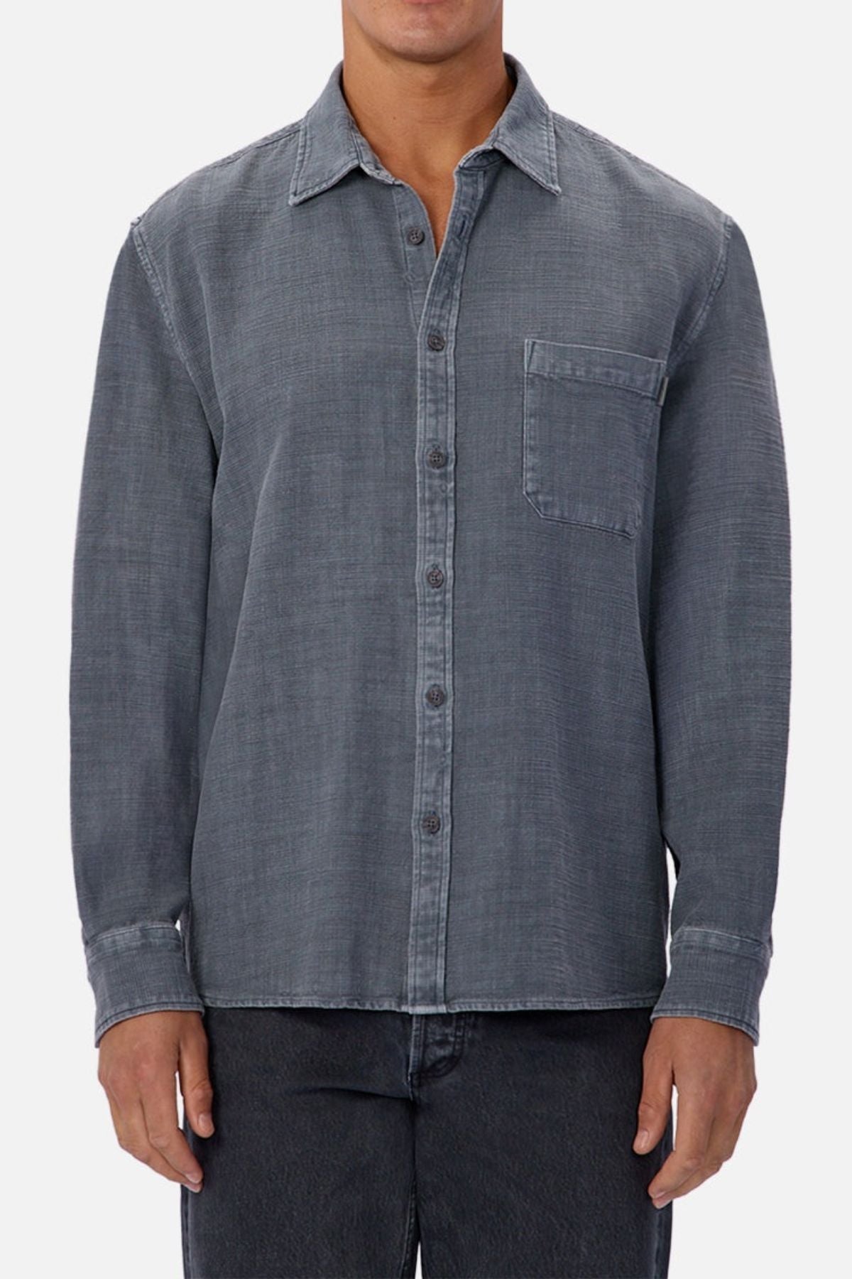 Someone stands against a plain background wearing the Industrie Lisbon Long Sleeve Shirt, featuring long sleeves, a classic collar, gray 100% cotton denim, and a chest pocket. Only their torso and upper legs are visible.