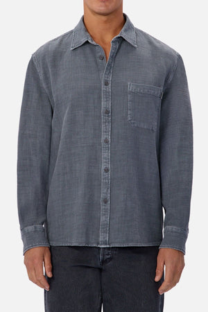 Someone stands against a plain background wearing the Industrie Lisbon Long Sleeve Shirt, featuring long sleeves, a classic collar, gray 100% cotton denim, and a chest pocket. Only their torso and upper legs are visible.
