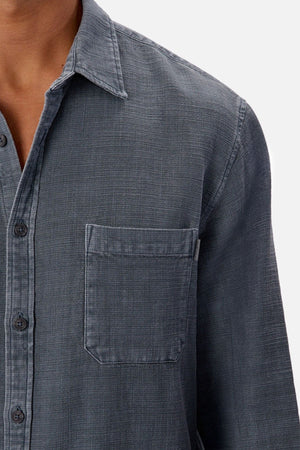 Close-up of a person wearing the Industrie Lisbon Long Sleeve Shirt in textured dark gray, featuring a classic open collar and front pocket. Shown from shoulder to mid-chest against a plain white background.