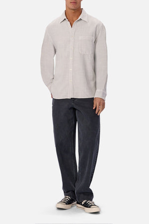 A person wearing the Industrie Lisbon Long Sleeve Shirt in light beige, featuring a classic collar and chest pocket, paired with loose dark jeans and black-and-white sneakers, stands against a plain white background.