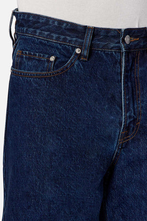 Close-up of a person's waist wearing the Industrie The Lone Star Jean in dark blue denim with orange stitching. The image highlights the front side of these baggy fit jeans, showcasing details such as the button, top of the zipper, front pocket, and belt loops. A white shirt is partially visible above these 100% cotton denim jeans.